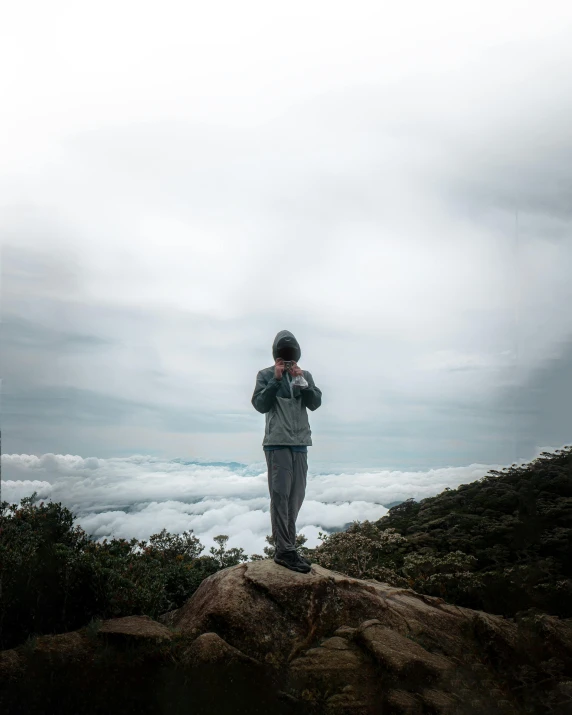 a person standing on top of a mountain holding a cell phone, on a cloudy day, photography], shrugging, trending photo