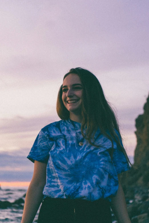 a woman standing on top of a beach next to the ocean, a portrait, unsplash, wearing a tie-dye t-shirt, portrait of teenage girl, blue, lachlan bailey