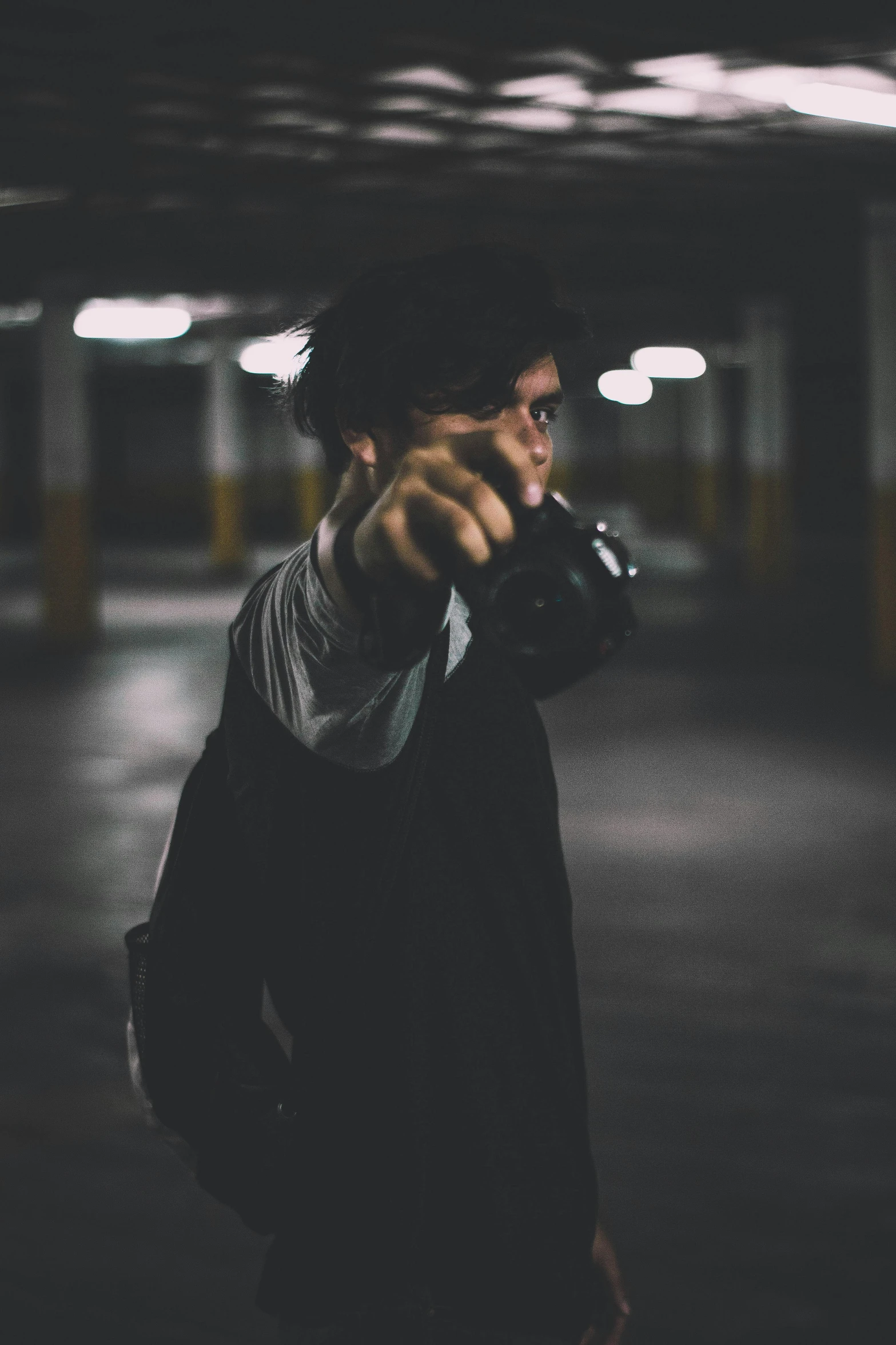 a man holding a camera in a parking garage, unsplash, visual art, fighting stance, ( ( theatrical ) ), holding pistol, declan mckenna