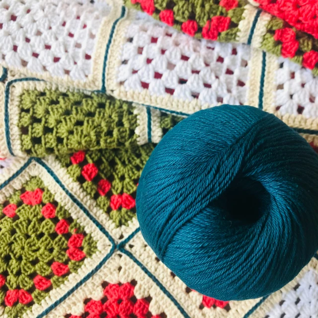 a ball of yarn sitting on top of a crocheted blanket, a cross stitch, by Sylvia Wishart, unsplash, arts and crafts movement, shades green and red, squared border, deep colour\'s, “berries