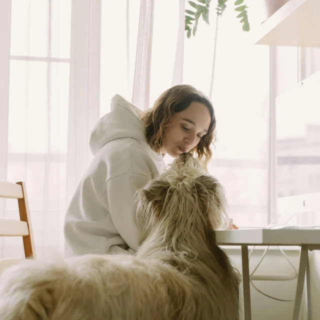 a woman sitting at a table with a dog, in a room, wearing an oversized hoodie, top selection on unsplash, fluffy full of light