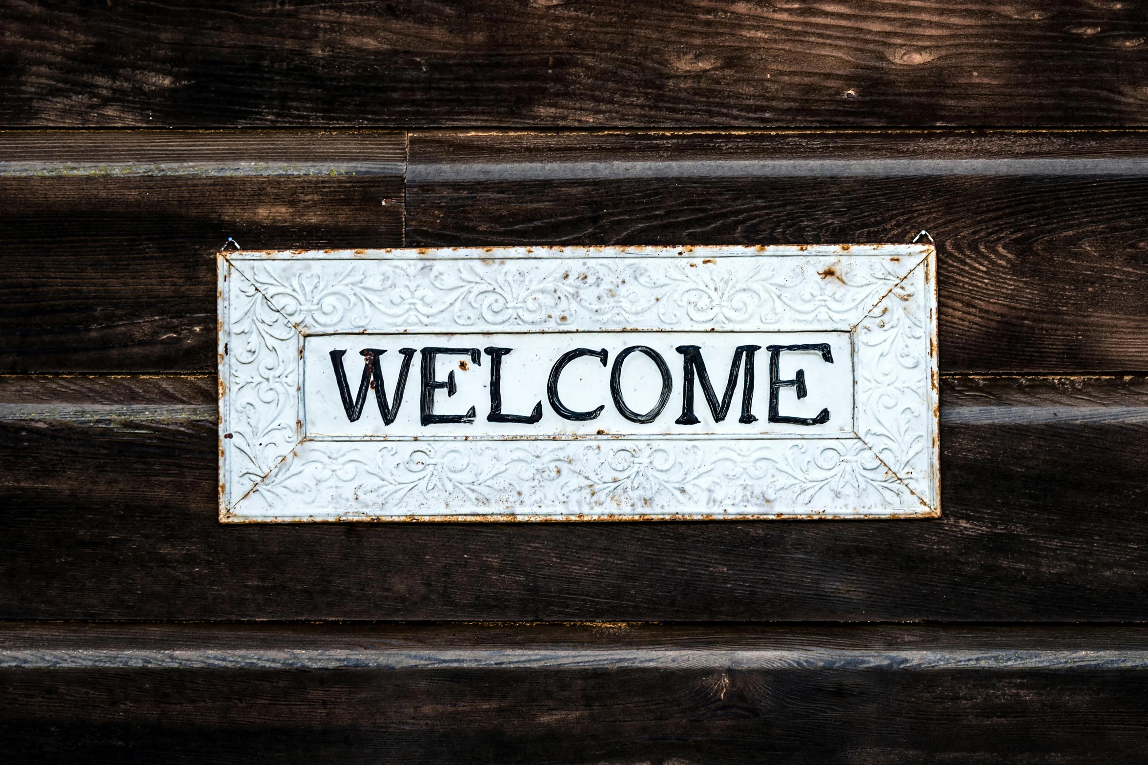a welcome sign sitting on the side of a wooden building, a picture, pexels, white metal, square, thumbnail, digital image