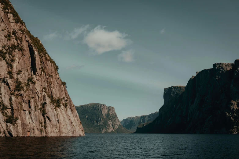 a large body of water with a mountain in the background, by Alexander Johnston, pexels contest winner, steep cliffs, quebec, slide show, grey