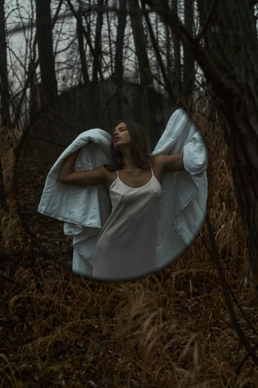 a woman laying on top of a bed in a forest, an album cover, inspired by Elsa Bleda, pexels contest winner, conceptual art, white cloth in wind shining, looking in a mirror, creepy pose, standing in moonlight