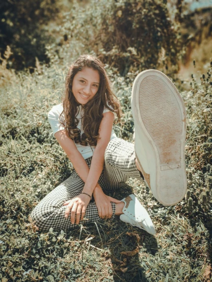 a woman sitting on top of a lush green field, a picture, by Emma Andijewska, pexels contest winner, wearing white sneakers, isabela moner, happily smiling at the camera, on a checkered floor