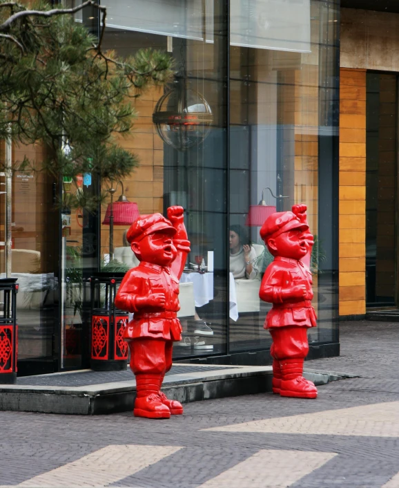 a couple of red statues sitting on the side of a road, a statue, inspired by Jeff Koons, pexels contest winner, hotel, mirror's edge in russia, three dwarf brothers, award winning shopfront design