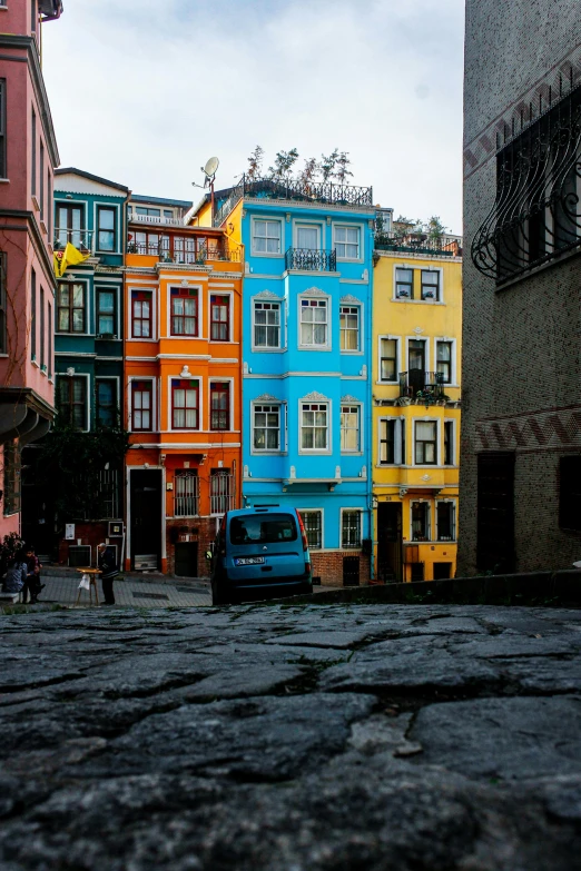 a car is parked on a cobblestone street, a colorized photo, inspired by Niyazi Selimoglu, unsplash contest winner, colorful houses, fallout style istanbul, built on a steep hill, colorful”