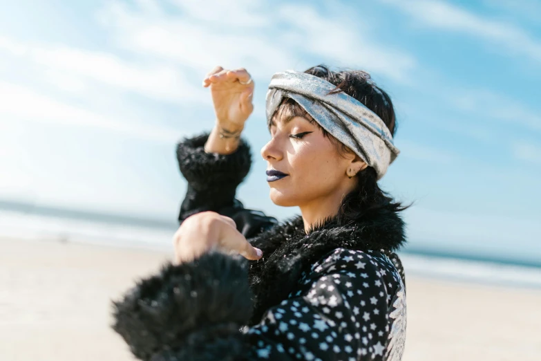 a woman standing on top of a sandy beach, an album cover, by Julia Pishtar, unsplash, graffiti, wearing a turban, shiny black lipstick, morena baccarin, patterned clothing