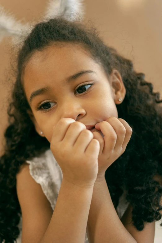 a little girl sitting at a table with a plate of food, unclipped fingernails, she has olive brown skin, thoughtful, close up of face