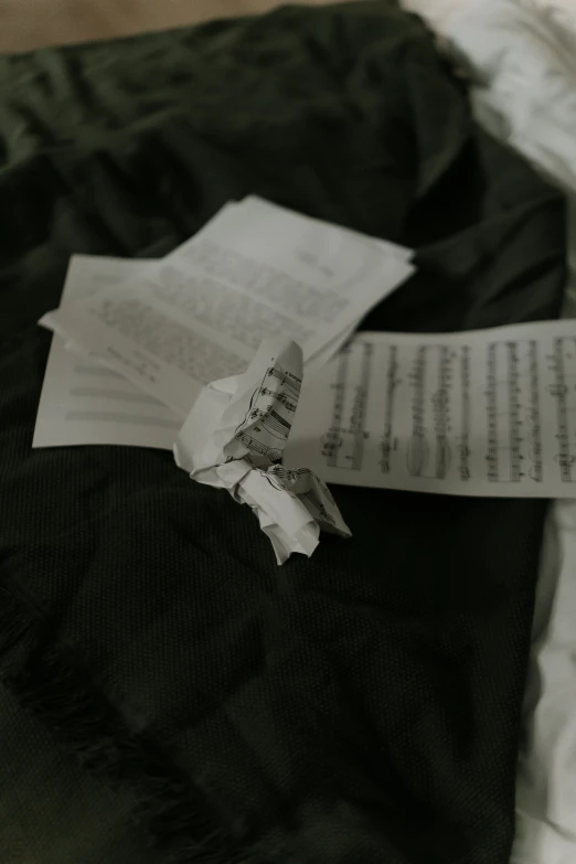 a piece of paper sitting on top of a bed, a black and white photo, by Song Xu, unsplash, happening, tattered wings, concert, damage, manuscript