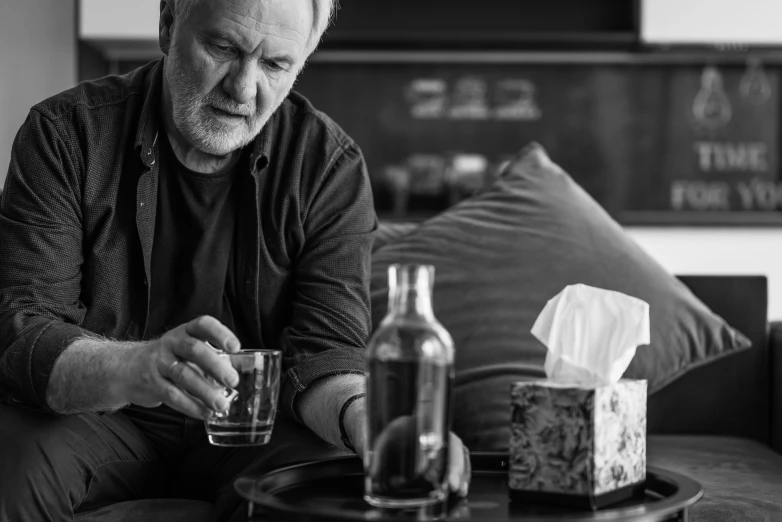 a man sitting on a couch holding a glass, by Adam Marczyński, visual art, anthony hopkins, drinking cough syrup, monochrome, on a table