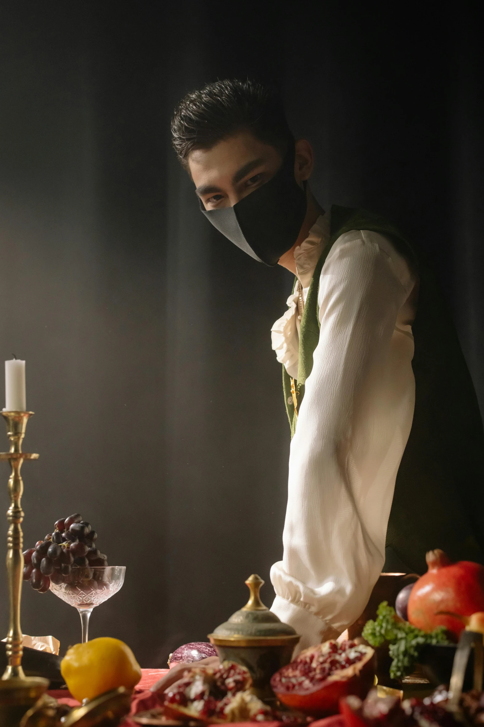 a man standing in front of a table filled with food, an album cover, inspired by Pietro Longhi, trending on pexels, renaissance, black mask, elegant victorian vampire, fashion shoot 8k, wearing facemask