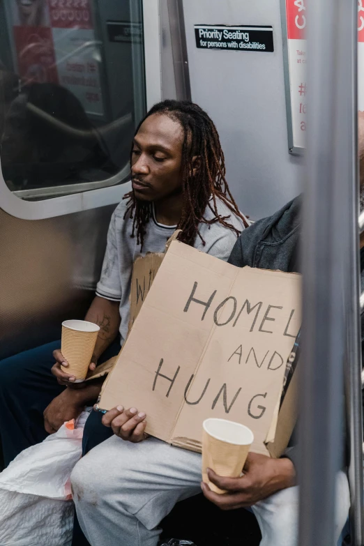 a man sitting on a subway holding a sign, trending on unsplash, hunger, someone in home sits in bed, makeshift houses, howard v brown