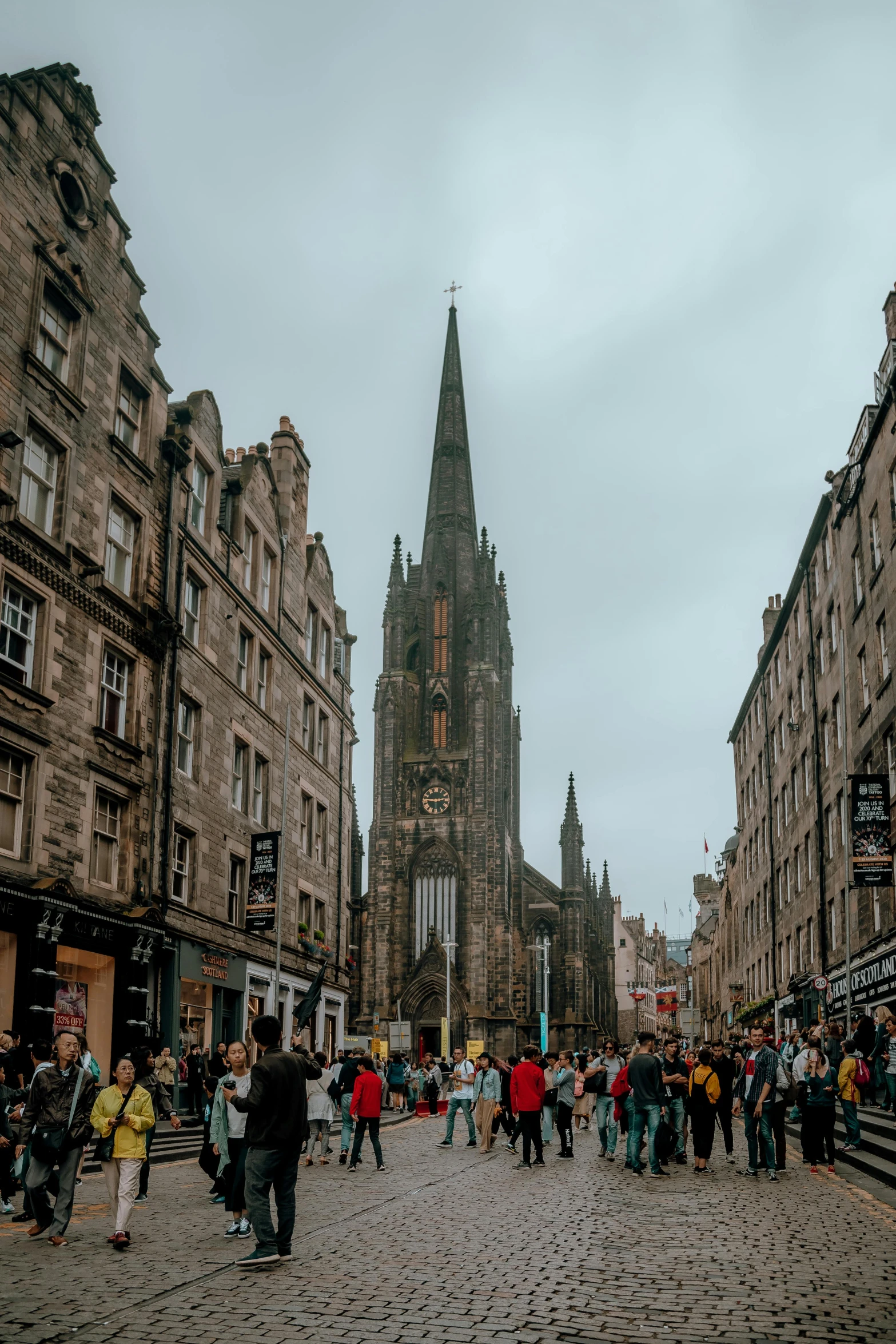 a group of people walking down a street next to tall buildings, gothic architecture, scottish, churches, stores