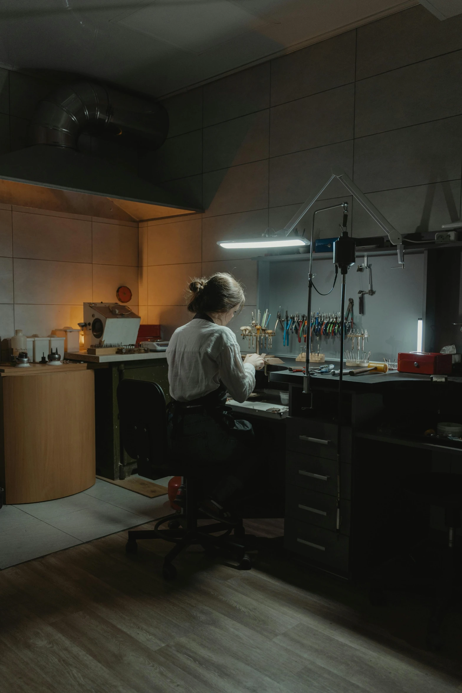 a man sitting at a desk in a dark room, experimenting in her science lab, jewelry lighting, manufacturing, daoshi