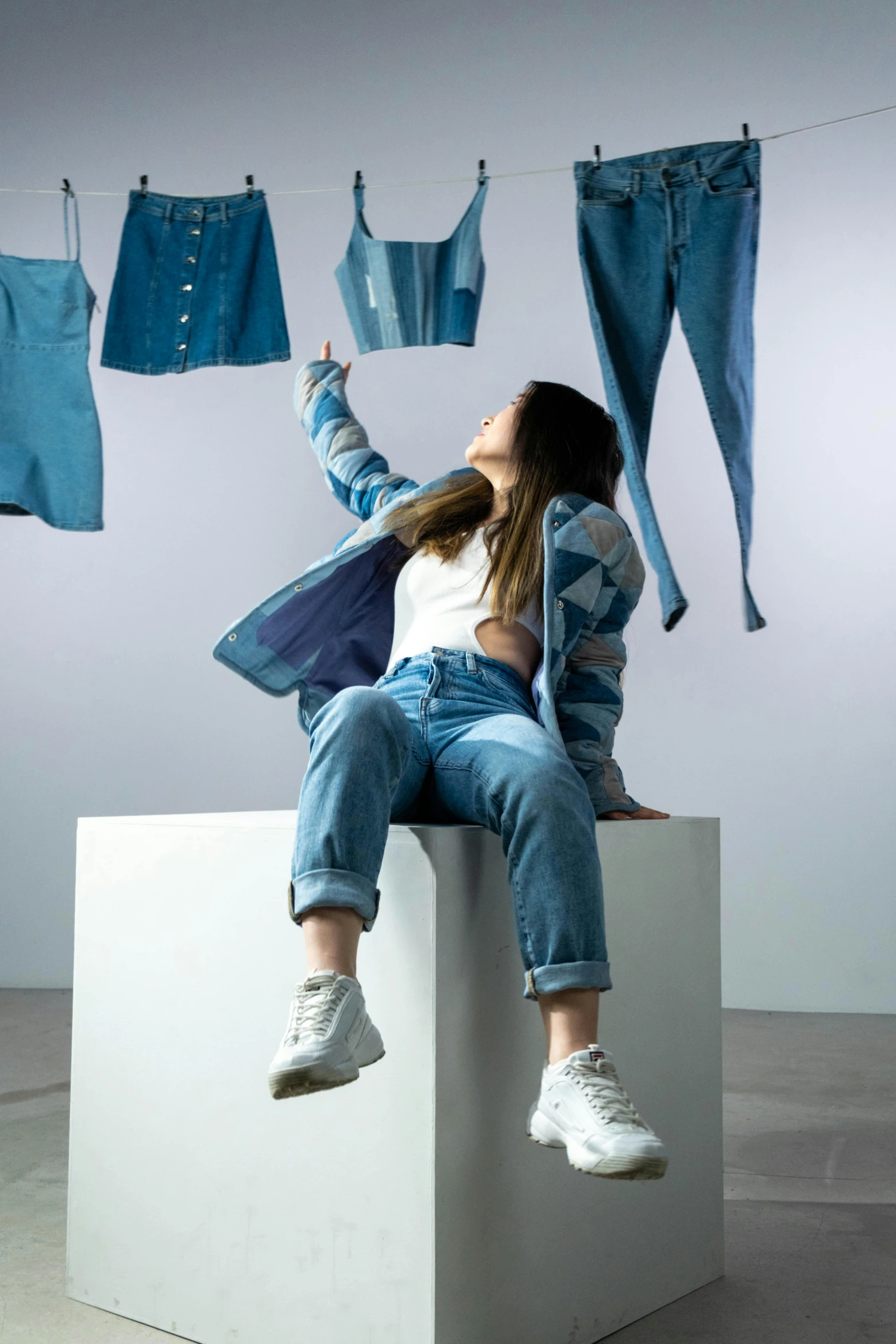 a woman sitting on top of a white cube, a picture, inspired by Kim Tschang Yeul, trending on pexels, denim jacket, hands in air, official store photo, sustainable materials