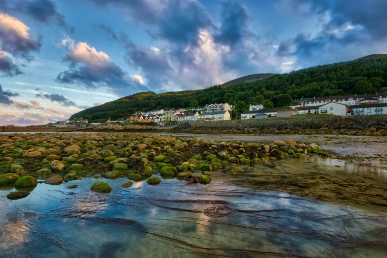 a large body of water sitting next to a lush green hillside, a picture, pexels contest winner, land art, on the beach at sunset, irish mountains background, quaint village, thumbnail