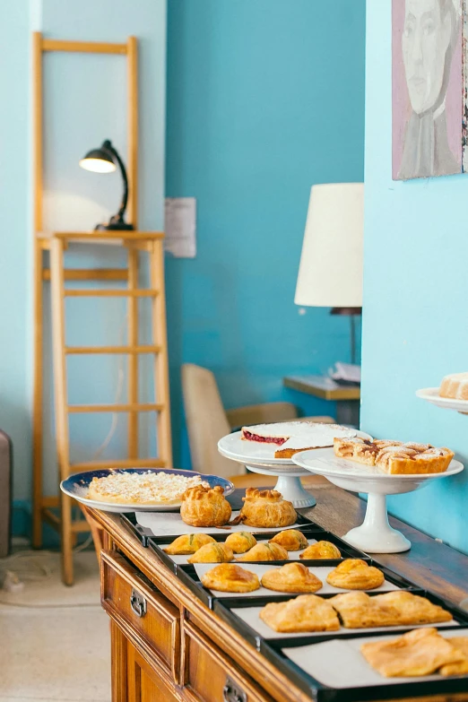 a table with a variety of pastries on it, brightly lit blue room, apartments, confortable atmosphere, pastel'