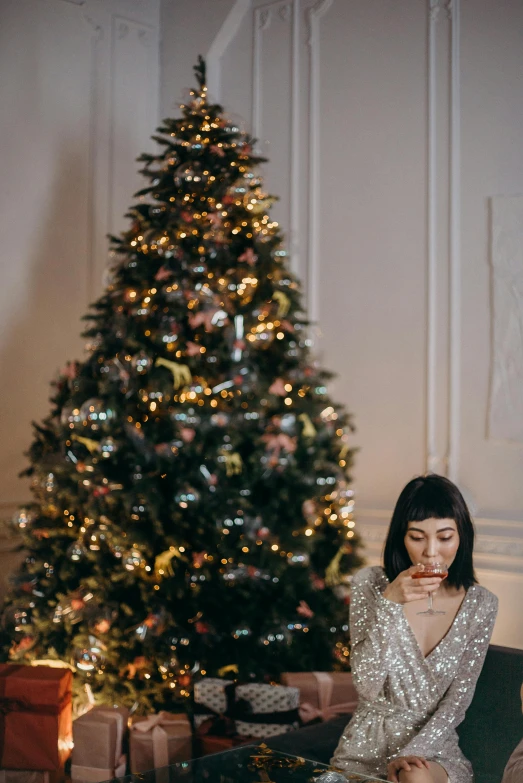 a woman sitting on a couch in front of a christmas tree, by Julia Pishtar, pexels contest winner, drinking champagne, kiko mizuhara, glitter gif, studio photo