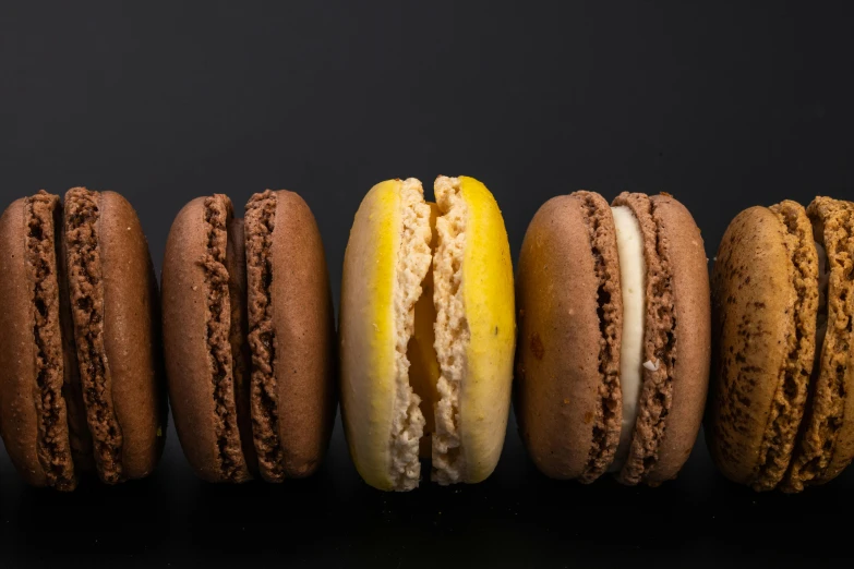 a row of macarons sitting next to each other, a portrait, brown, yellow, high-contrast, product shot