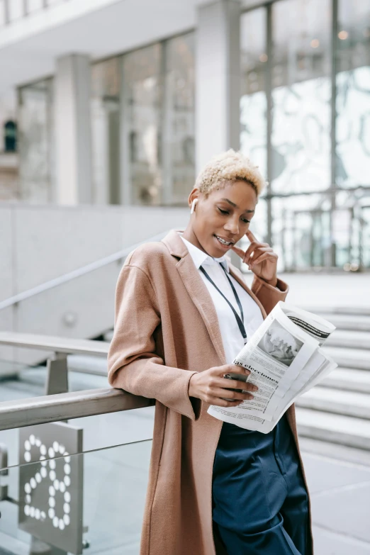 a woman talking on a cell phone while holding a newspaper, trending on pexels, short blonde afro, business suit, light brown coat, ad image