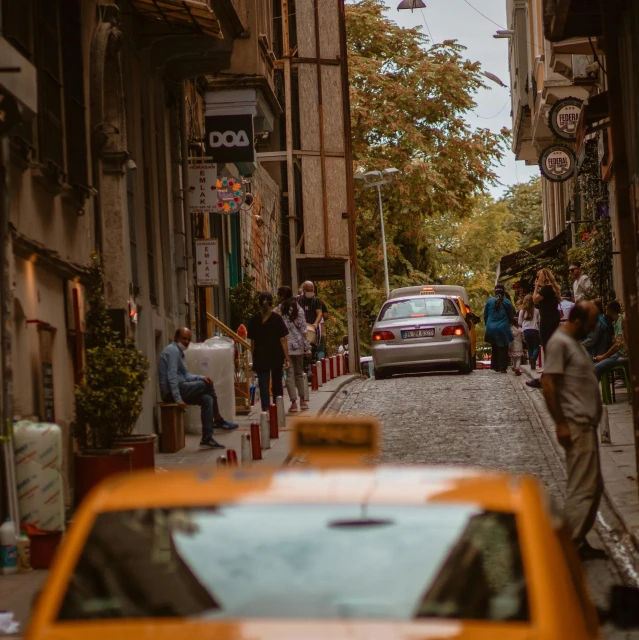 a yellow taxi driving down a street next to tall buildings, by Cafer Bater, pexels contest winner, istanbul, people watching around, standing in an alleyway, brown