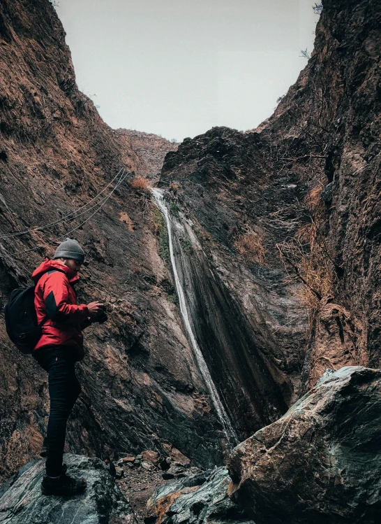 a man in a red jacket standing in front of a waterfall, a picture, pexels contest winner, in socotra island, cinematic photo 4k, taking a picture, extreme narrow