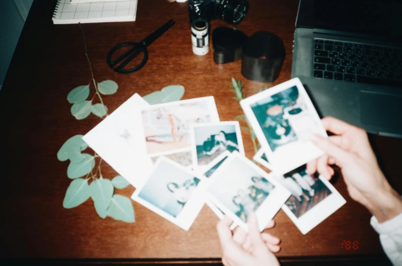 a person holding polaroids on top of a wooden table, inspired by Elsa Bleda, unsplash, process art, with a bunch of stuff, computer aesthetic, botanicals, 90's photo