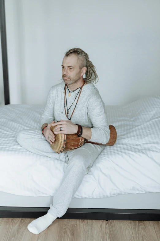 a man sitting on a bed with a guitar, inspired by Peter Madsen, trending on pexels, renaissance, in a white boho style studio, shpongle, drummer, sitting on a log