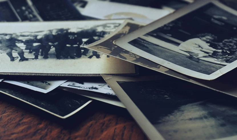 a pile of old photos sitting on top of a wooden table, by Lucia Peka, unsplash, desaturated, miscellaneous objects, photograph ”