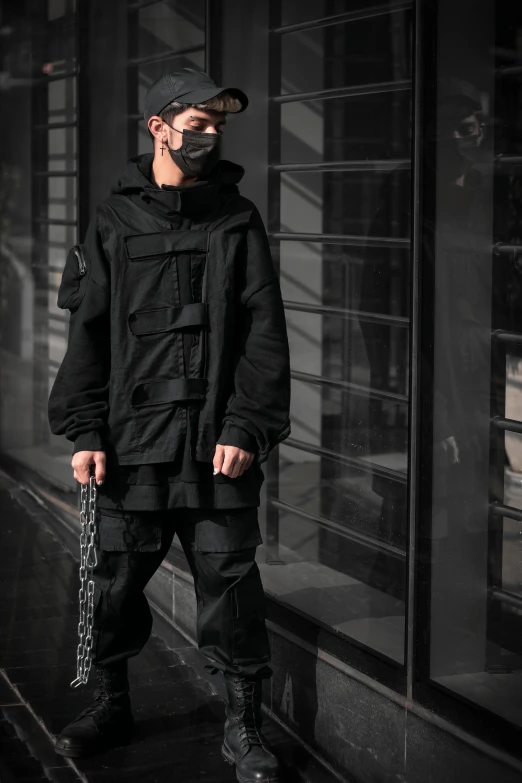 a man standing on a sidewalk with a chain around his neck, inspired by Gang Hui-an, unsplash, visual art, wearing space techwear, with two front pockets, wearing a dark hood, wearing tactical gear