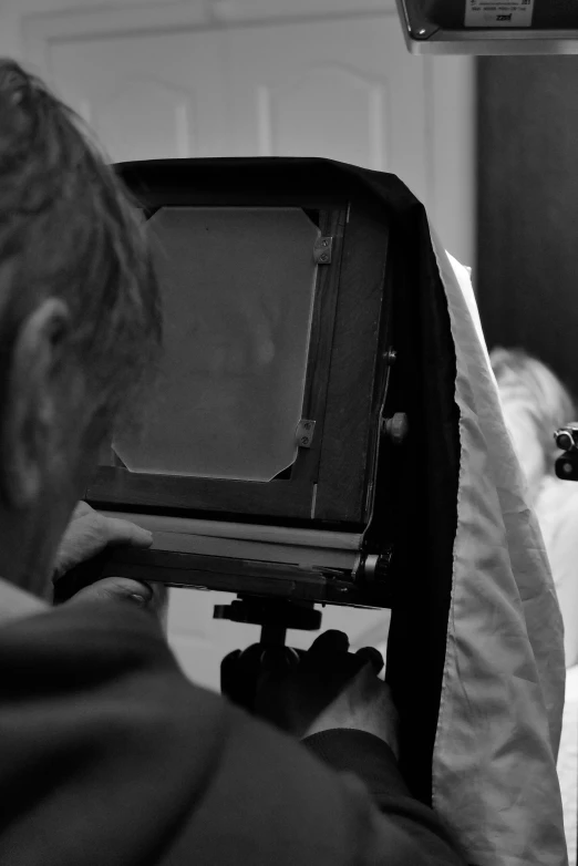 a black and white photo of a man holding a camera, inspired by Arnold Newman, video art, back - shot, arriflex, close up to the screen, colour photograph