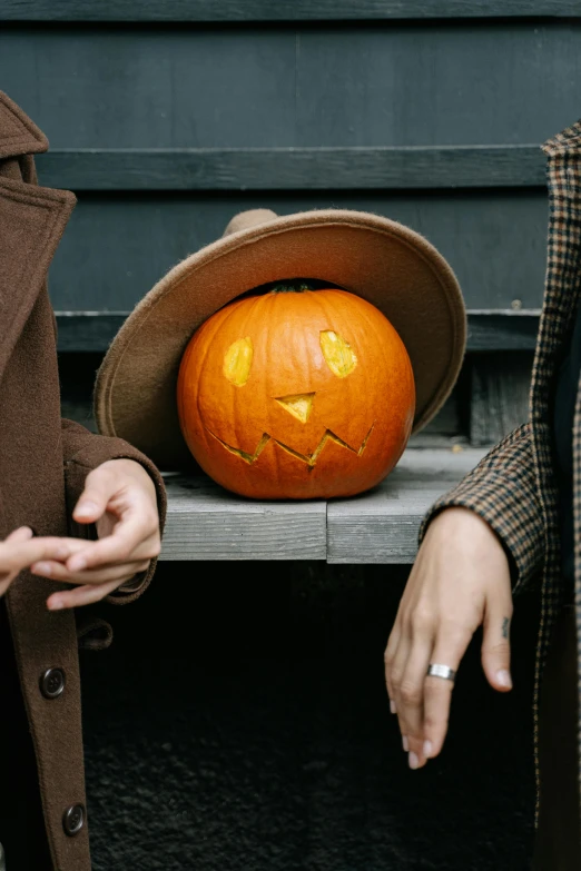 a couple of people standing next to a pumpkin, pexels contest winner, brown hat, sleek hands, flirting, dark. no text