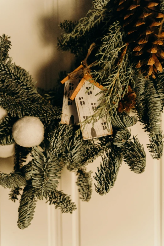 a close up of a wreath on a door, by Julia Pishtar, fir trees, a cozy, detailed white, indoor