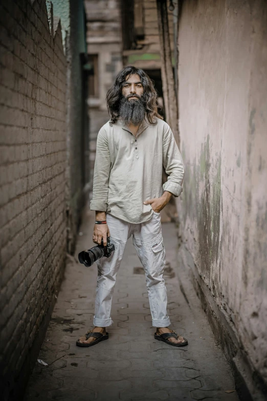 a man standing in an alley with a camera, by Peter Churcher, long ashy hair, india, full body 8k, portait image