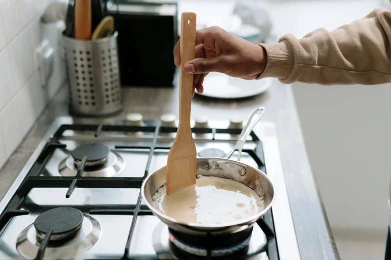 a person stirring something in a pot on a stove, trending on pexels, cream, holding a wood piece, lightly dressed, thumbnail
