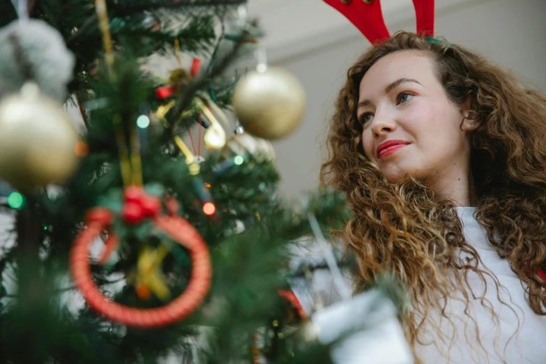 a woman standing in front of a christmas tree, pexels contest winner, happening, avatar image, young woman looking up, close - up photo, decoration