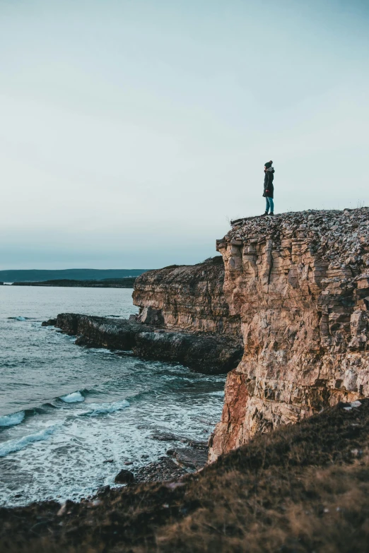 a person standing on a cliff overlooking the ocean, strong features, ultrawide image, 2019 trending photo, dramatic”