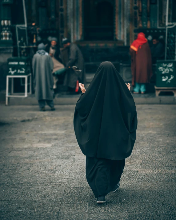 a woman in a black veil walking down a street, trending on unsplash, unilalianism, non-binary, he is in a mosque, dressed in a robe, instagram photo