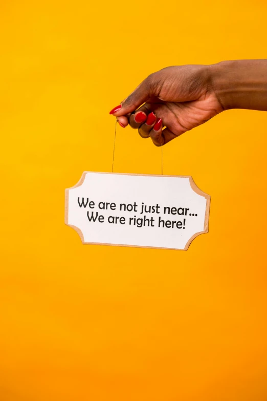 a woman holding a sign that says we are not just near we are right here, pexels, yellow backdrop, instagram post, full product shot, hanging