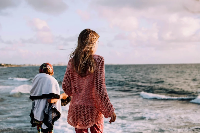 a couple of people standing on top of a beach, pexels contest winner, bright red cape on her back, girl looking at the ocean waves, patterned clothing, gif