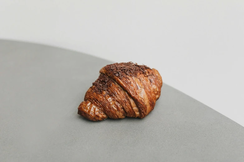 a close up of a croissant on a table, by Simon Gaon, unsplash, photorealism, hand carved brown resin, 3/4 front view, charred, momoshiki ōtsutsuki