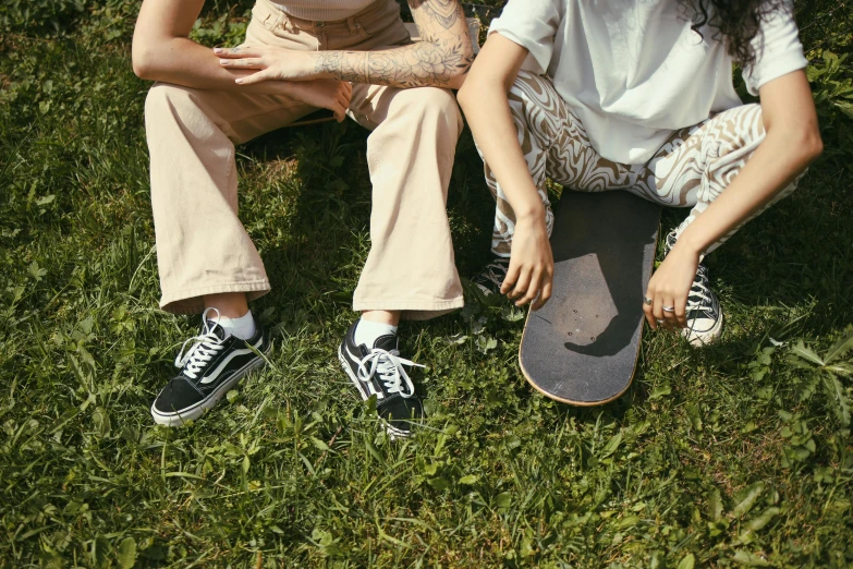 a couple of people sitting on top of a lush green field, trending on pexels, realism, detailed skateboard, pants, off - white collection, lesbian