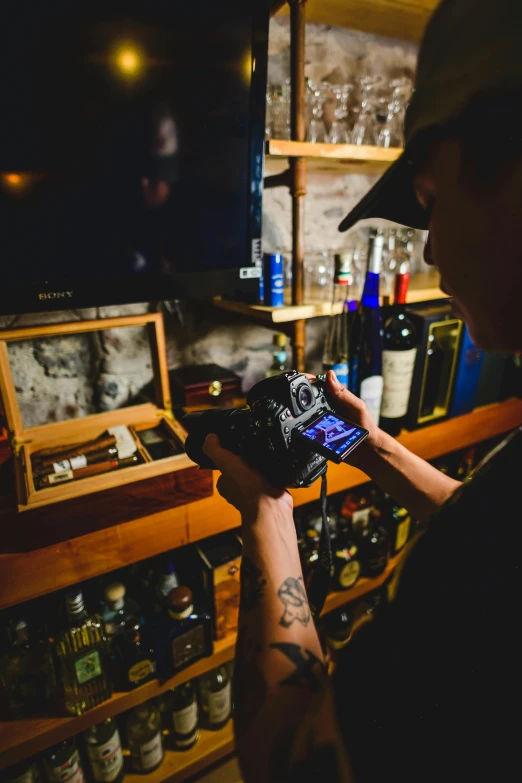 a man standing in front of a bar holding a camera, tattooed, whiskey, inspect in inventory image, holding a camera