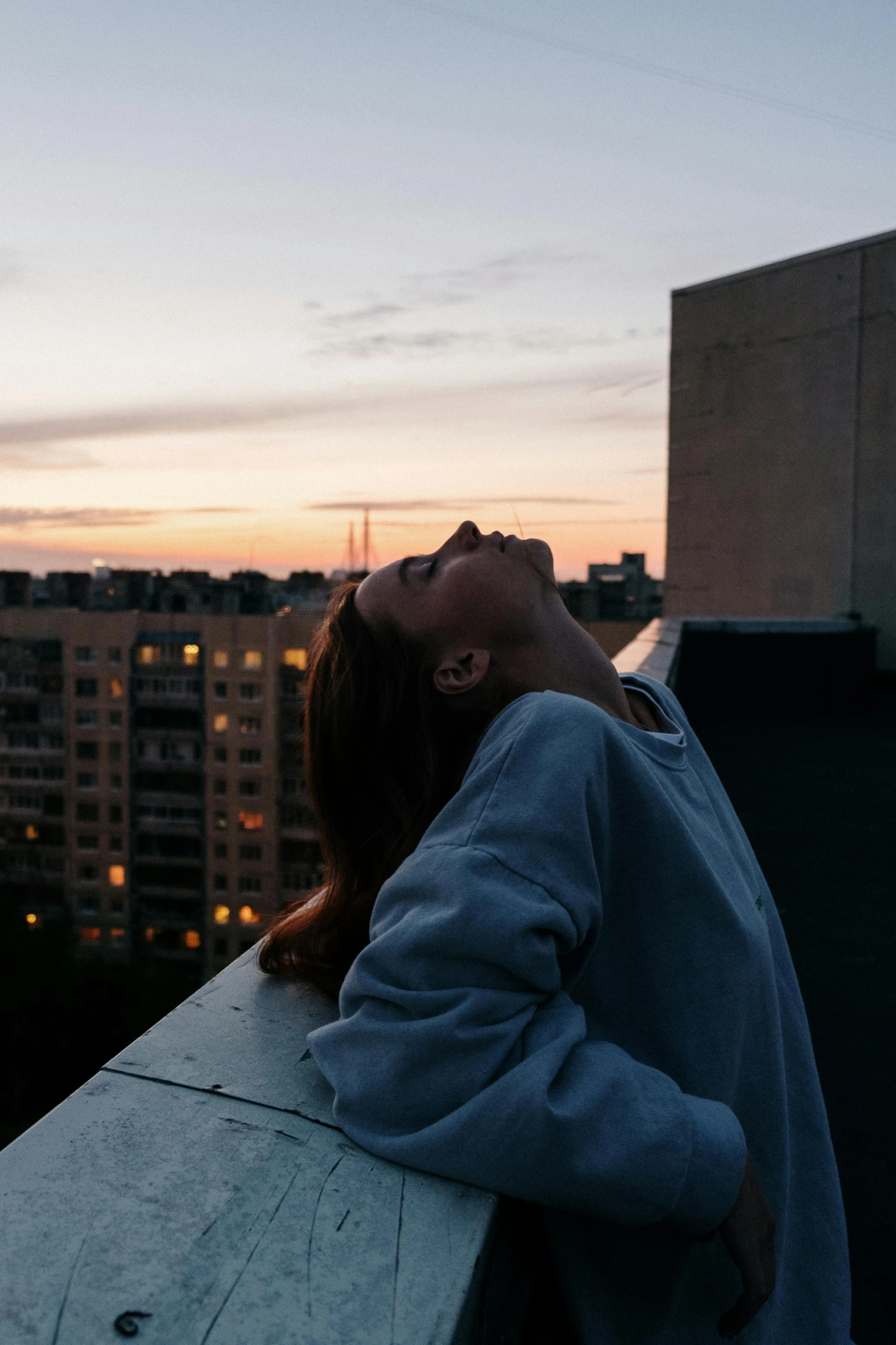 a woman that is laying down on a ledge, inspired by Elsa Bleda, trending on pexels, happening, evening sky, proud looking away, from the roof, head bowed slightly