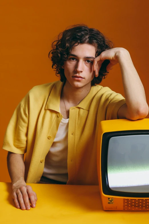 a man sitting in front of a yellow television, joe keery, official store photo, curls on top, early 2 0 0 0 s