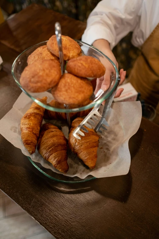 a person sitting at a table with a plate of croissants, bowl filled with food, high-quality photo, thumbnail, at the counter