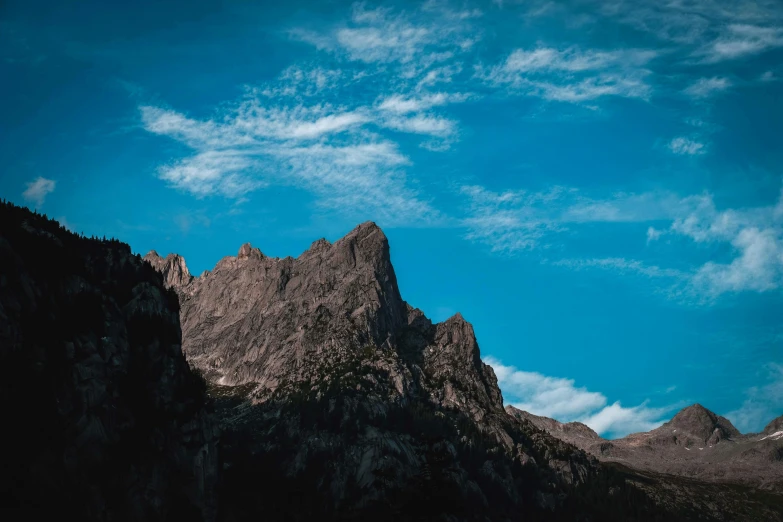 a mountain range with a blue sky in the background, towering, unsplash photography, dark-skinned, craggy