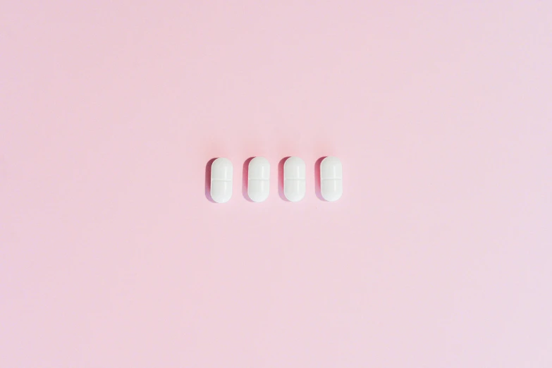 a couple of pills sitting on top of a pink surface, by Emma Andijewska, antipodeans, sleek white, in a row, flatlay, threes