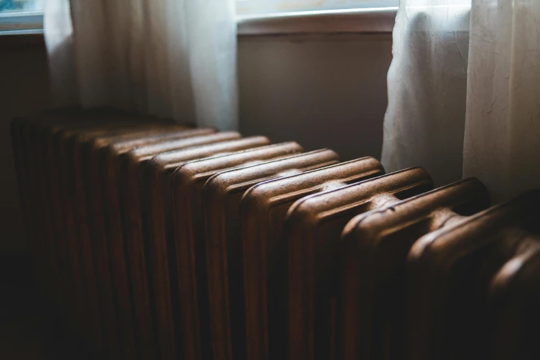 a radiator sitting in front of a window next to a curtain, inspired by Elsa Bleda, pexels contest winner, old copper pipes, in a row, muted brown, reading